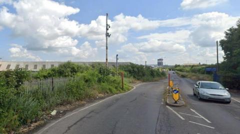 A Google Images screengrab of Dawes Lane, where the incident took place. There is a road leading to an industrial area, buildings can be seen in the background, with cars and vegetation in the foreground.