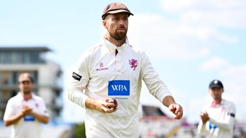 Jack Leach walks off the outfield at Taunton holding the ball in his right hand