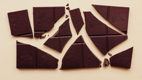 A dark chocolate bar broken into pieces on a beige background