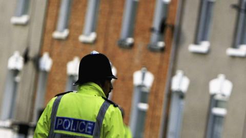 A police officer in a high-viz jacket stood in front of terraced houses