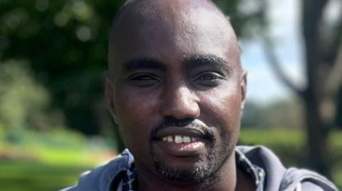 A close-up of a man in a park who is looking directly at the camera