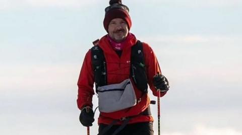 Stephen Chamberlain pictured wearing a red jacket and wool hat. He's wearing black gloves and holding what looks to be sticks to aid trekking