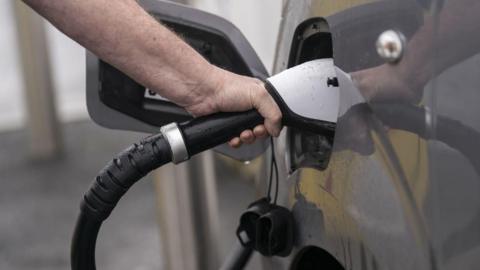 A close-up of someone's hand placing an EV charger into the side of car.