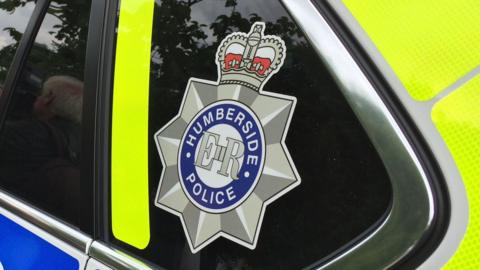 A close up of a police car, with the emblem of Humberside police on the back rear passenger window.