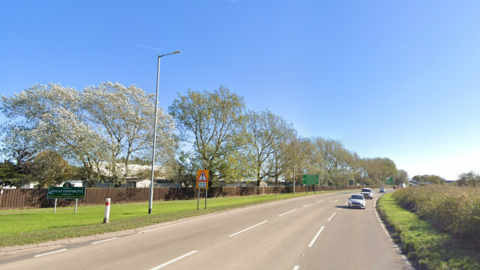 A generic image of the road close to a holiday park in Great Yarmouth where the incident has happened. You can see cars on the road and the tops of caravans behind a fence and tree-lined verge.