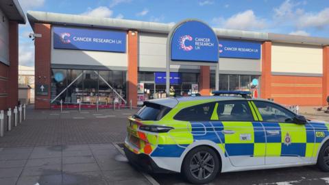 A police car outside the Cancer Research UK store. A cordon has been set up around the building.