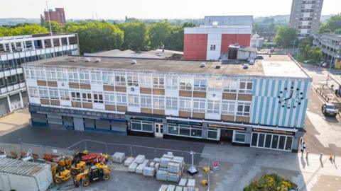 An aerial view of Market Square in Harlow, showing a concrete building with construction materials being set up in front of it.