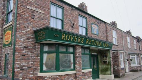 The green front sign, door and windows on the Rovers Return Inn pub on the new set of the ITV soap Coronation Street. On a bricked building joined to terraced housing. 