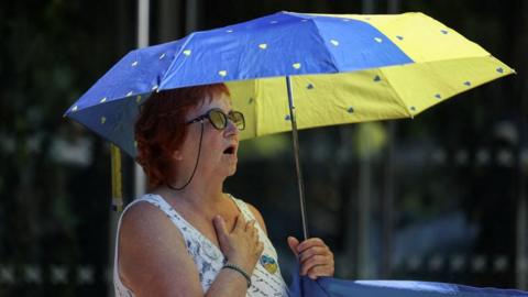 A woman standing under a blue and yellow umbrella