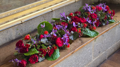 A floral display in various colours on a wood and stone platform.