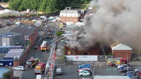 Aerial shot of fire appliances tackling a fire with billowing smoke.