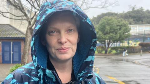 Heather Anderson is wearing a patterned waterproof with a hood over her head. She has blue eyes and blonde hair. 