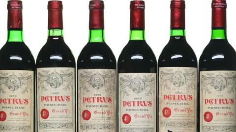 A row of six red wine bottles. The labels on them say "PETRUS"
