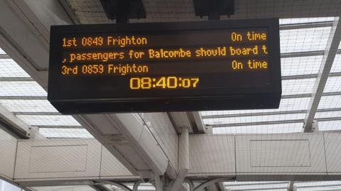 A black departures board at a train station. In orange two trains are listen both with the destination of "Frighton"
