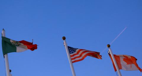 Mexican, American and Canadian flags wave from flagpoles against a blue sky