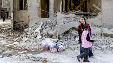 A woman and child walk by a damaged building, struck days earlier, during the U.S.Israeli military campaign on March 4, 2026 in Tehran, Iran.