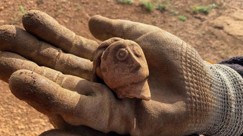 A decorative flagon in the shape of a woman’s head being held in the open palm of a person's hand.