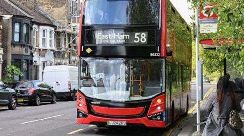 A red double decker bus, no 58, at a bus stop. A woman walks towards it.