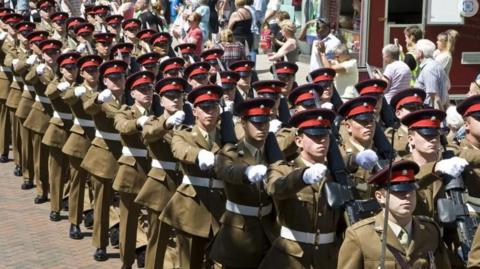 A group of soldiers wearing khaki -coloured military uniform marching in unison