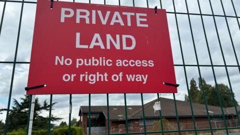 A red sign tied to a green fence which reads: 'PRIVATE LAND No public access or right of way'. 