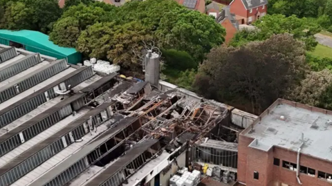 A picture taken with a drone, showing part of the fire-damaged factory, with homes behind it, divided by trees.