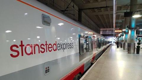 A white and grey train at a platform with the words "Stansted Express" on the side.
