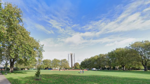 General view of London Fields, showing grass, trees and a high rise in the background.