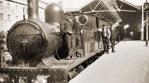 A black and white image of a steam train with some men standing next to engine and others on a platform.