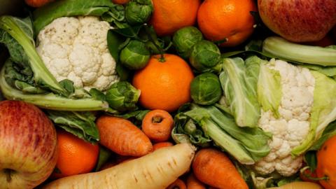 A selection of colourful fruit and veg stacked in a box on top of one another.