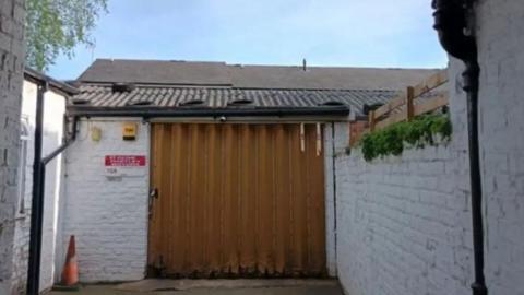 A white painted brick building with a brown corrugated sliding door.