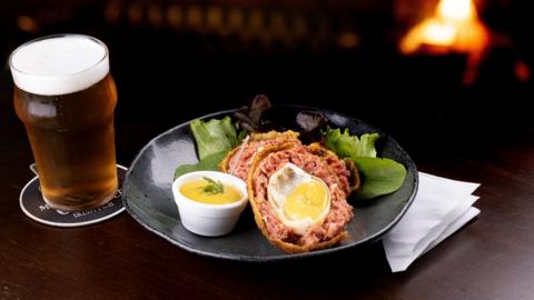 A salad and Scotch egg on a plate next to a pint of beer