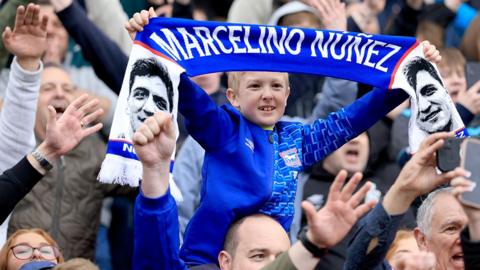Young Ipswich Town fan holds blue and white Nunez scarf above his head