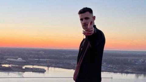 Lewis Stevenson pointing to the camera on top of a tall chimney in Riga, Latvia