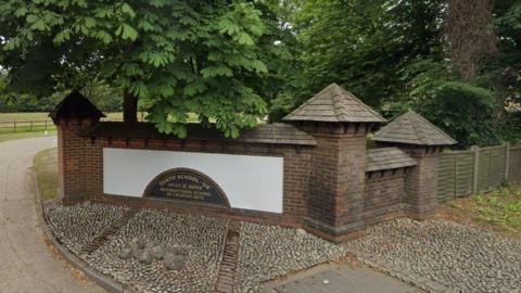 The entrance to ISCA, the International School of Creative Arts, in Wexham, Buckinghamshire, showing a white and black sign, and a brick gate wall by the entrance 