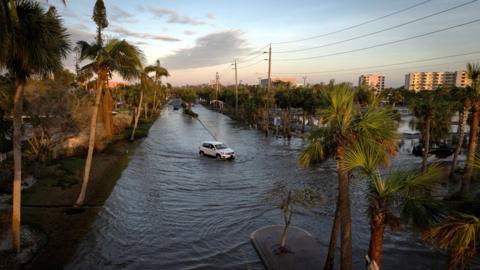 A car driving through a flooded street following Hurricane Milton in Siesta Key, Florida