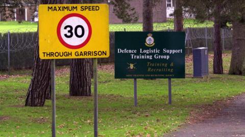 The entrance to the barracks. A 30mph sign next to a green sign saying "Defence Logistic Support Training Group".