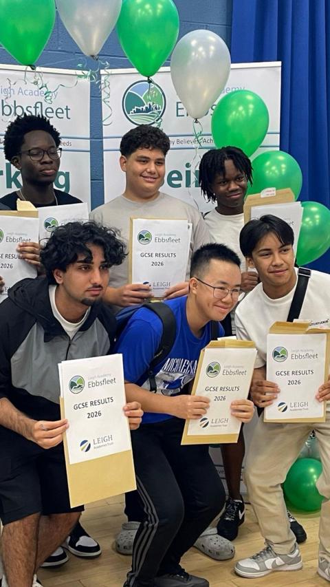 Six teenagers holding certificates with GCSE results indoors surrounded by balloons