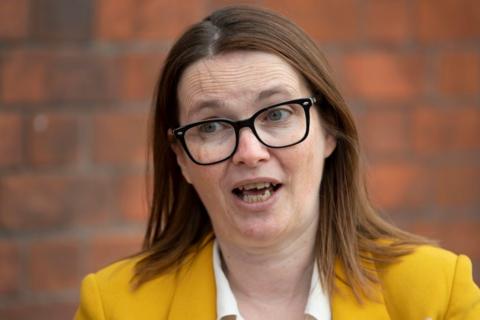 A woman talking. Former politician Kirsty Williams has black framed glasses on and short light-brown hair. She has a yellow jacket on, under which is a white shirt.