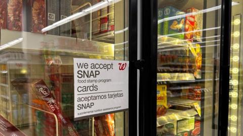 A frozen aisle in a grocery store shows a sign on the door reading "we accept Snap food stamp program cards".
