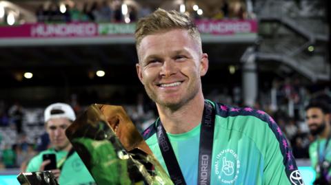 Oval Invincibles captain Sam Billings smiles as he holds up The Hundred trophy