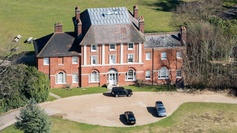 An aerial shot of Forest Lodge in Windsor Great Park, showing a large redbrick country manor house with pillars and cars parked out the front.