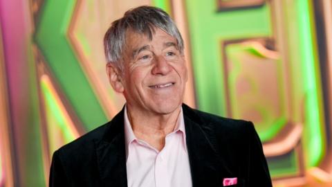 Stephen Schwartz at the "Wicked: For Good" New York Premiere held at Lincoln Center for the Performing Arts. He wears an open-neck pink shirt and black blazer.