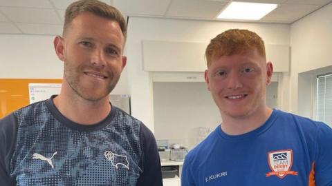 Student in blue top and ginger hair stood with Derby County defender, Callum Elder