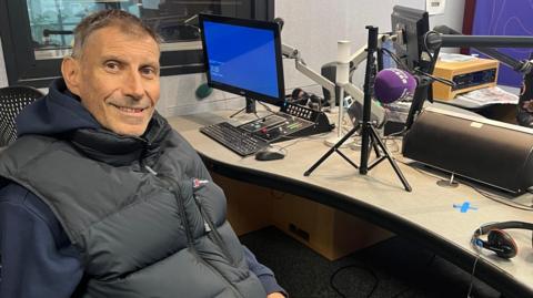A picture of Keith Todd inside the BBC Radio Sussex studio in Brighton with Sarah Gorrell. Keith is wearing a black Berghaus gilet.