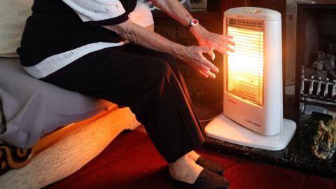 Pensioner holding their hands against electric heater