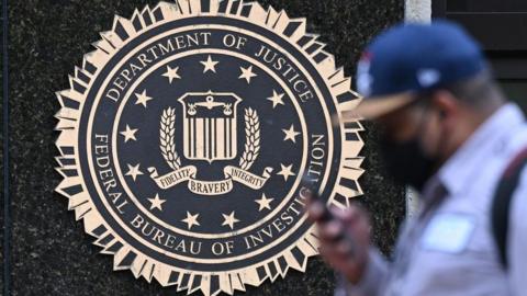 A pedestrian walks past a seal reading "Department of Justice Federal Bureau of Investigation", displayed on the J. Edgar Hoover FBI building, in Washington, DC, on August 15, 2022