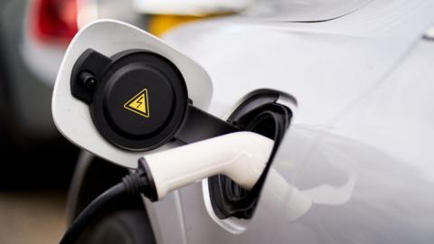 A white electric car with a white charger plugged in to it.