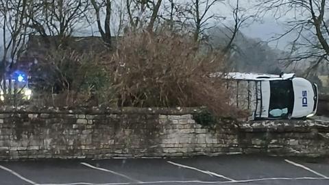 A stone bridge with a white van on its side and a police vehicle with its blue lights flashing