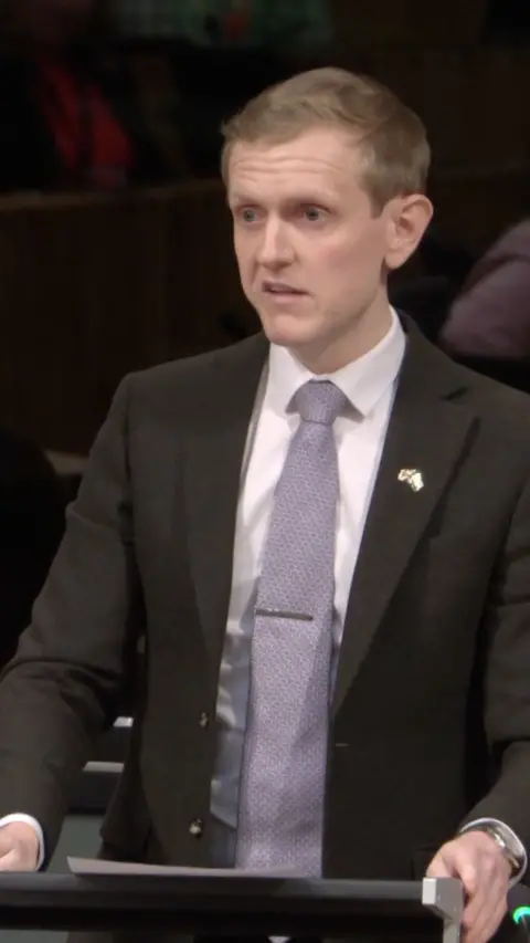 Joe Martin speaking at a lectern in the Senedd.