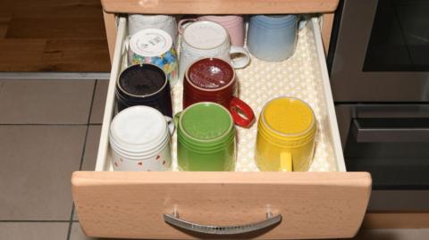 A number of mugs in an open drawer of a kitchen unit